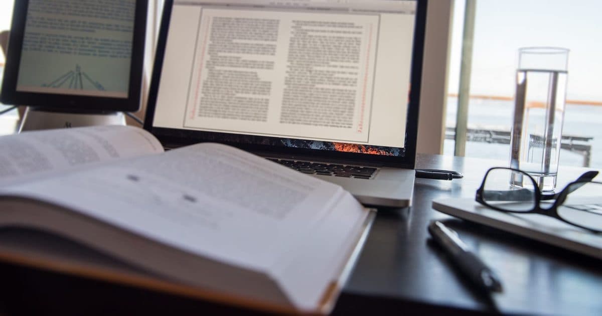 Open textbook and laptop on a study desk beside a window
